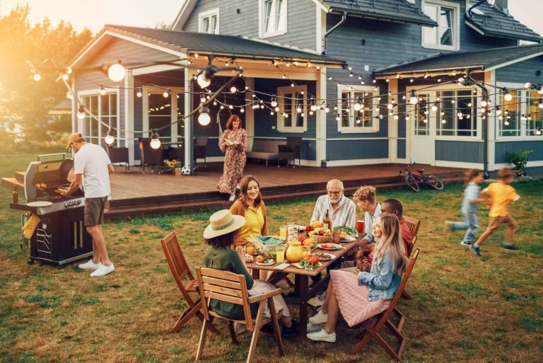 a group of people sitting around an outdoor table in front of a house