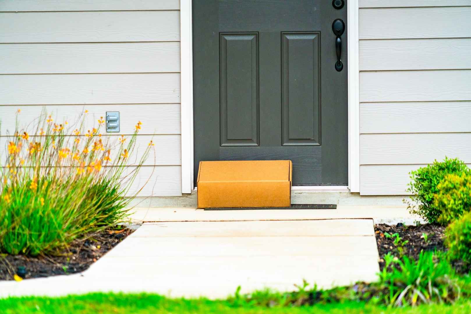 A box is delivered to the doorstep of a house, placed on the welcome mat in front of a dark gray door.