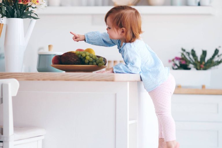 curious infant baby girl trying to reach things on the table in the kitchen with the help of step stool