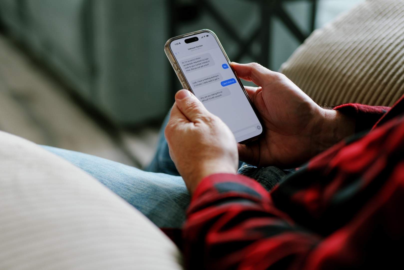A person in a red and black plaid shirt holds a smartphone and reads a text message conversation.