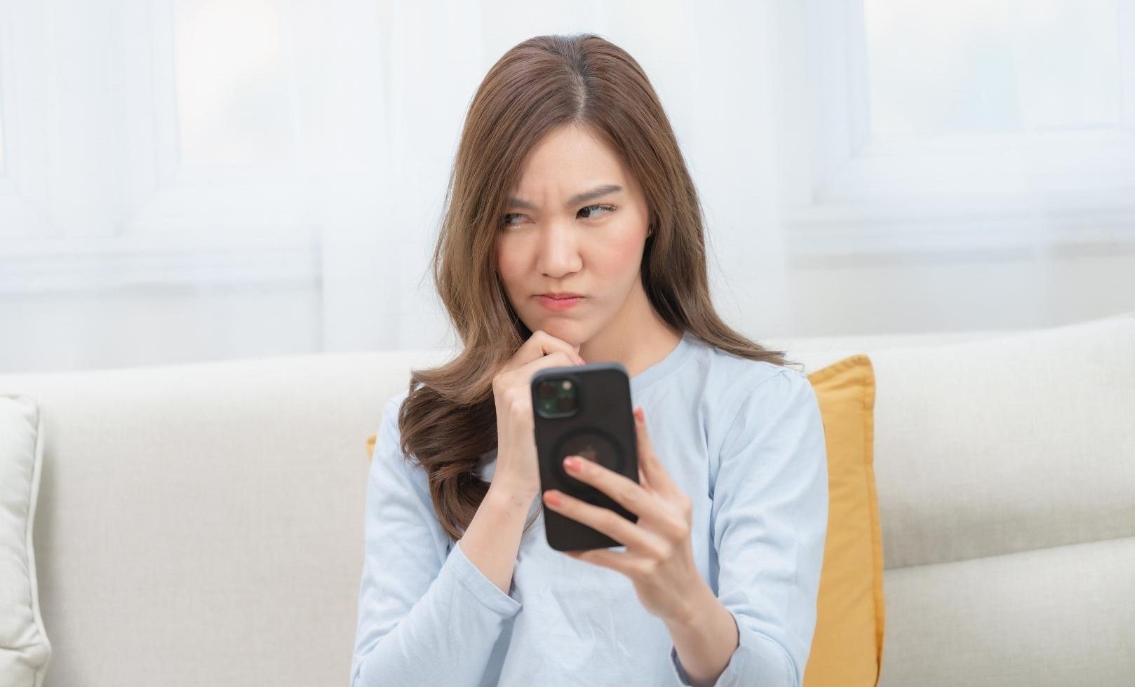 A person is sitting on a couch and looking at their phone with a confused expression.