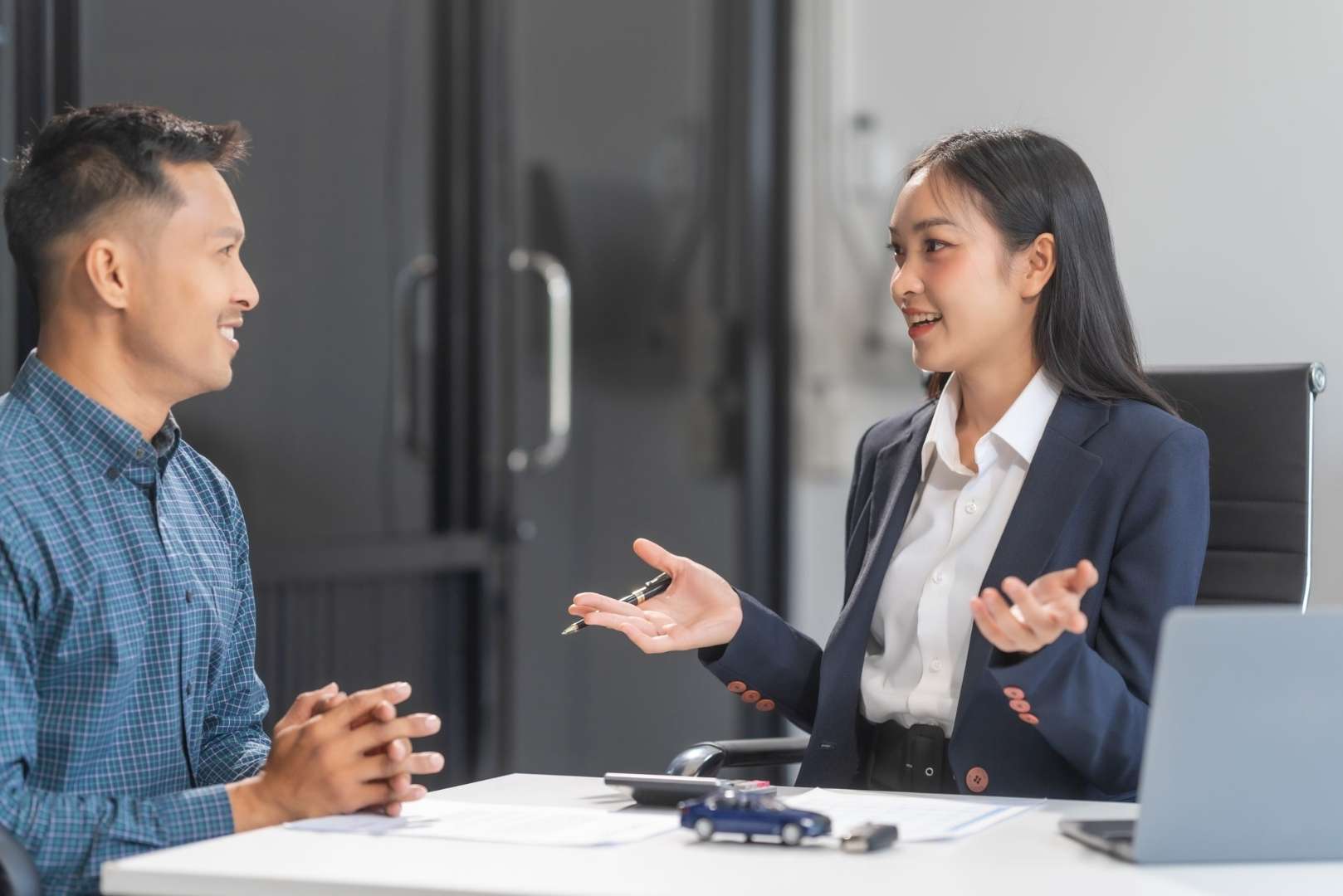 A man sits across from a woman gesturing with her hands while discussing something at a desk.