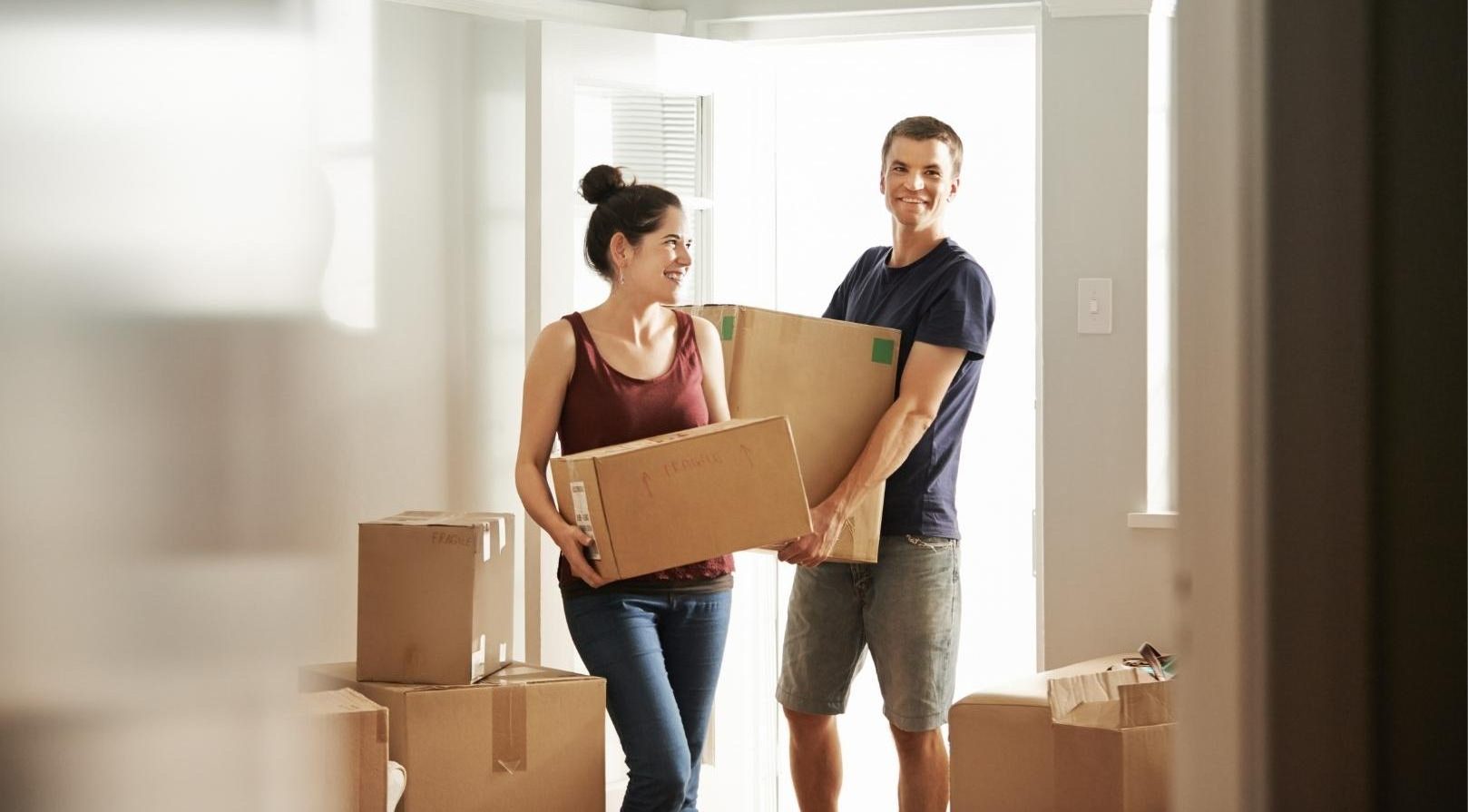 A smiling couple carrying boxes into new home.